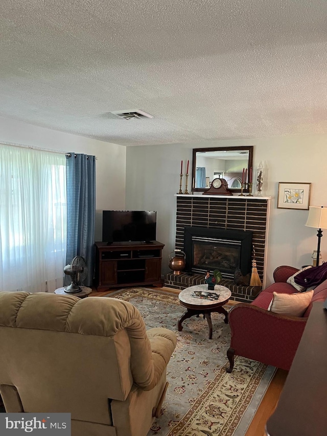 living room with a brick fireplace, visible vents, a textured ceiling, and wood finished floors