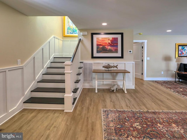 stairs with recessed lighting, wainscoting, a decorative wall, and wood finished floors