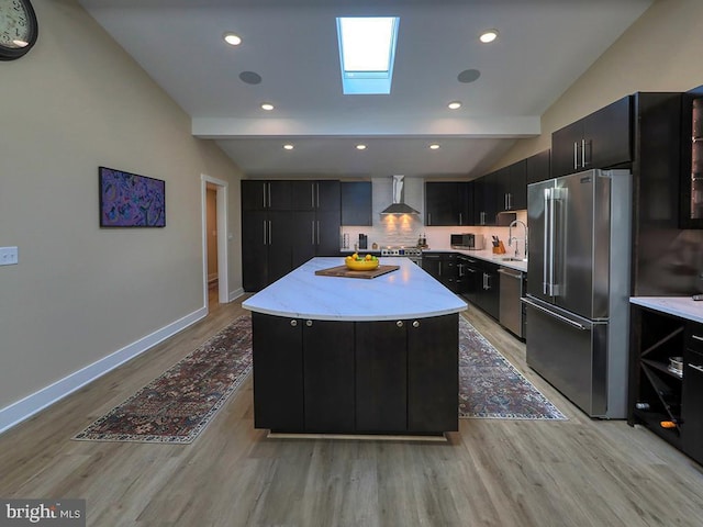 kitchen with wall chimney exhaust hood, appliances with stainless steel finishes, and dark cabinetry