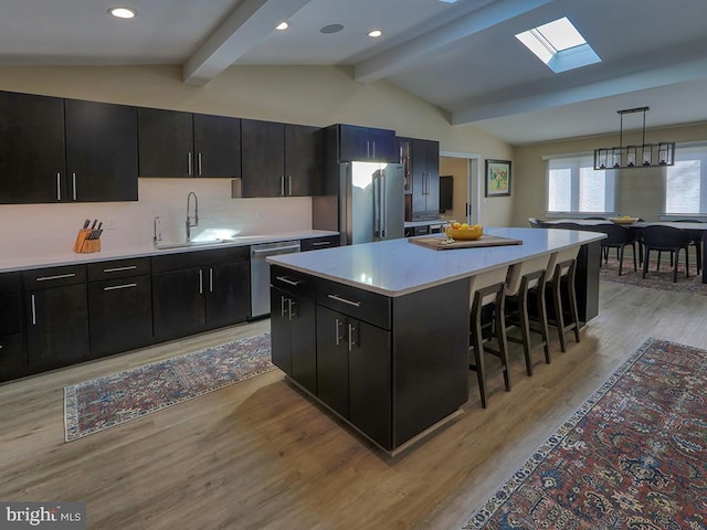 kitchen featuring dark cabinets, a sink, appliances with stainless steel finishes, lofted ceiling with skylight, and a kitchen bar