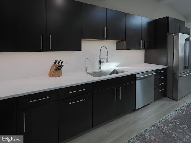 kitchen featuring light wood finished floors, appliances with stainless steel finishes, a sink, and dark cabinets