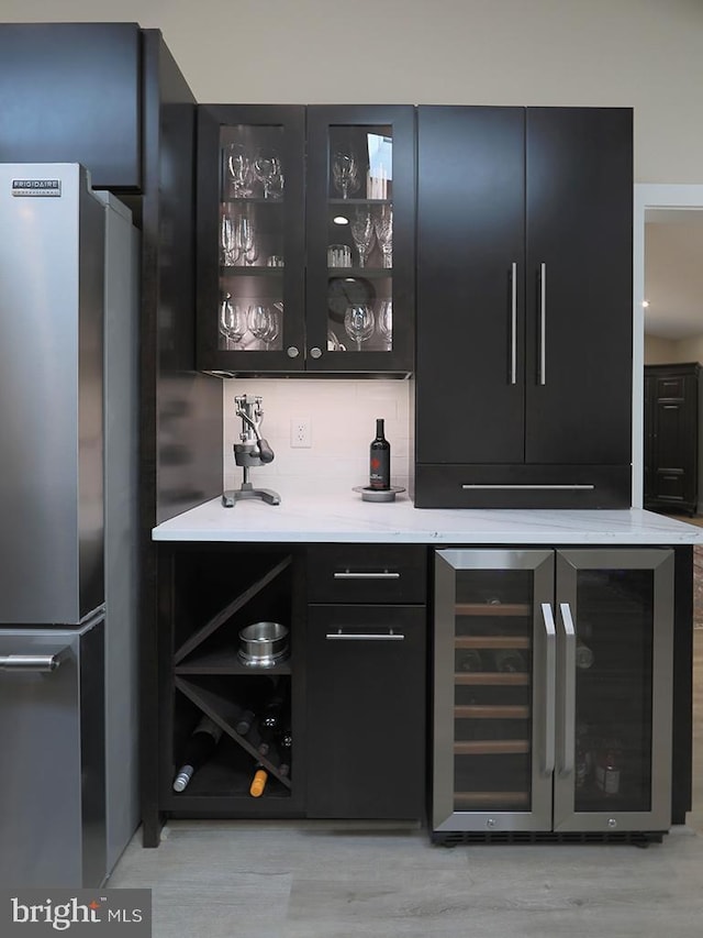 bar featuring wine cooler, a dry bar, tasteful backsplash, freestanding refrigerator, and light wood-type flooring