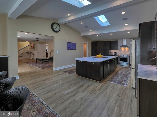 kitchen with vaulted ceiling with skylight, wall chimney exhaust hood, stainless steel appliances, light countertops, and light wood-style floors