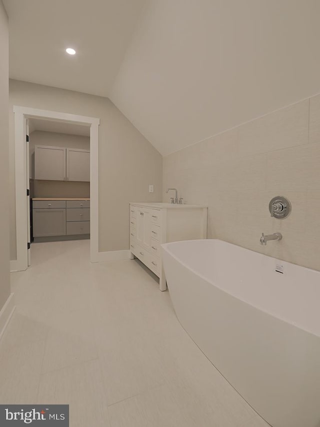 bathroom featuring lofted ceiling, a freestanding tub, vanity, and baseboards