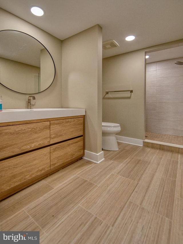 bathroom with recessed lighting, toilet, vanity, tiled shower, and baseboards