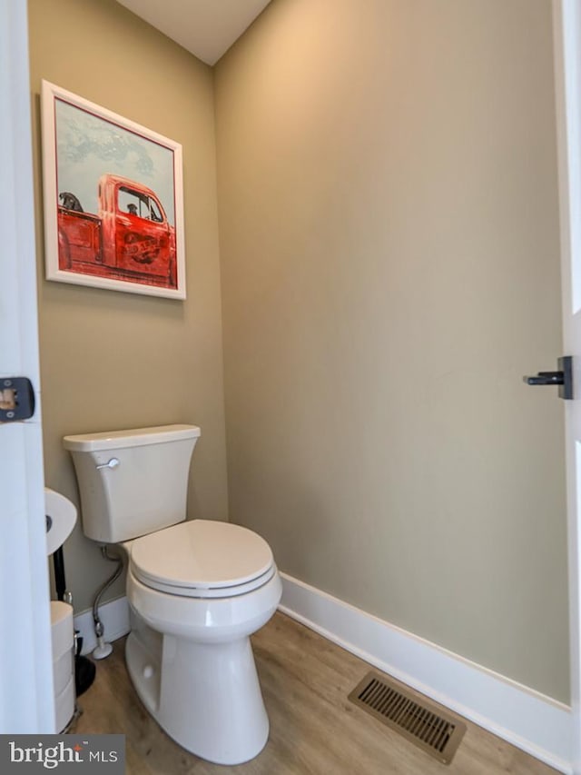 half bathroom with toilet, wood finished floors, visible vents, and baseboards