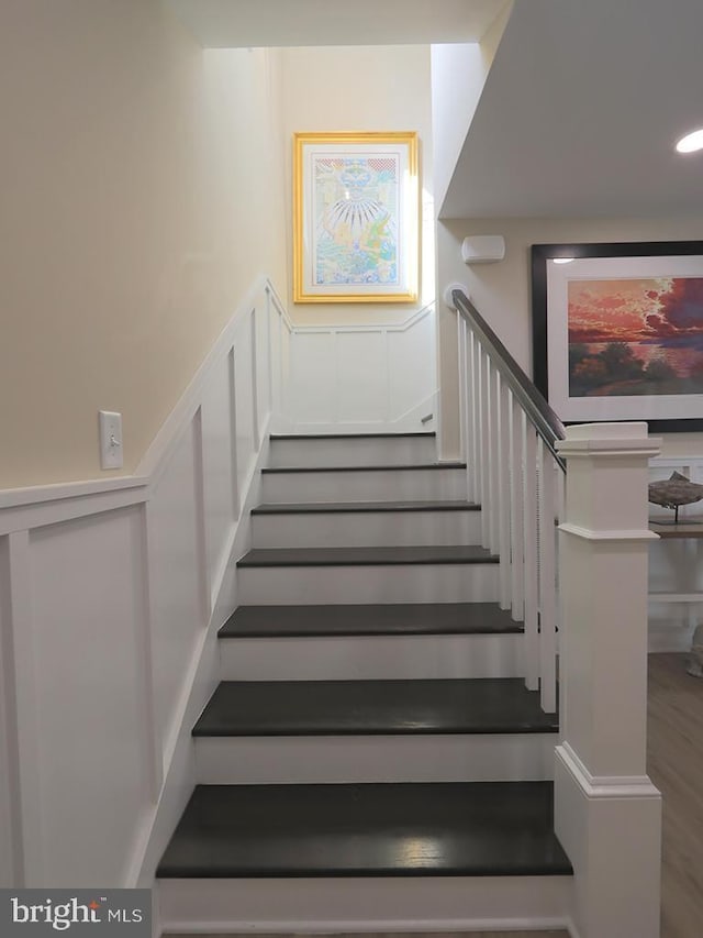 stairway featuring a decorative wall, wood finished floors, and wainscoting