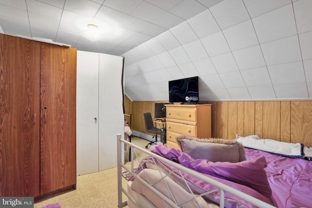 bedroom featuring vaulted ceiling, wooden walls, and light floors