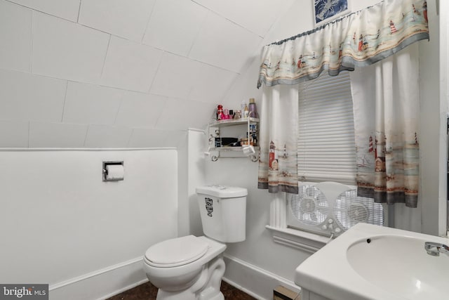 half bathroom with lofted ceiling, toilet, a sink, and baseboards