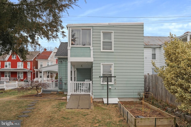 rear view of house featuring a garden, fence, and a lawn