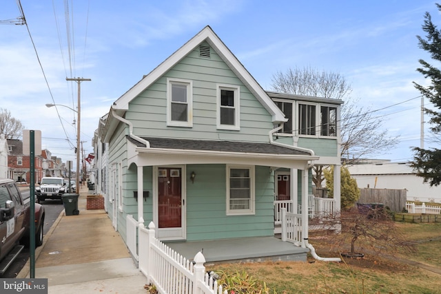 view of front facade featuring a shingled roof, covered porch, and fence