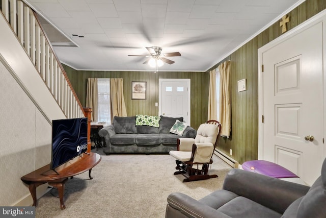 carpeted living room featuring stairs, baseboard heating, a ceiling fan, and crown molding