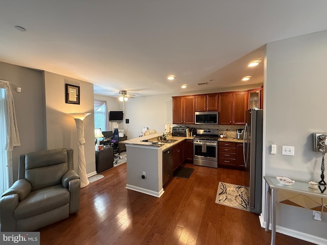 kitchen featuring dark wood-style floors, appliances with stainless steel finishes, open floor plan, a peninsula, and a sink