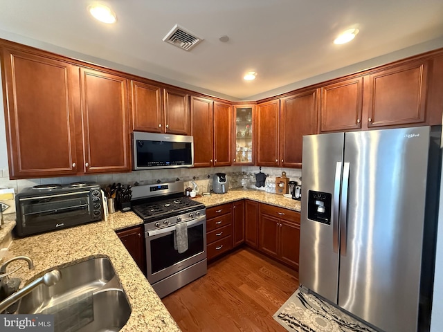 kitchen with stainless steel appliances, a sink, visible vents, dark wood finished floors, and glass insert cabinets