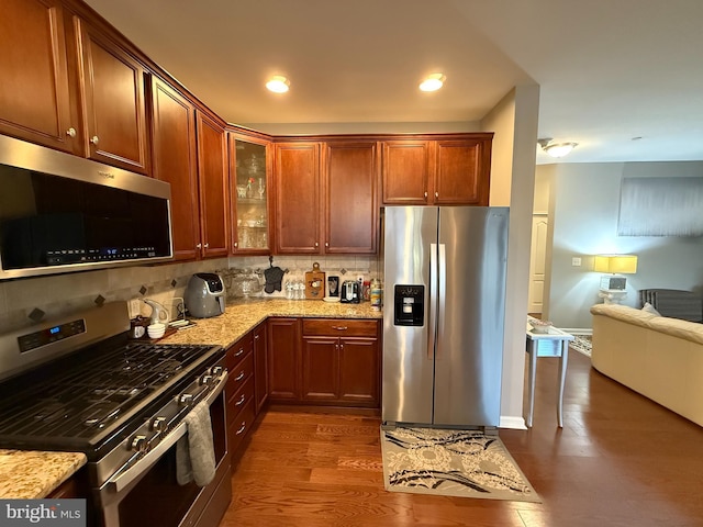 kitchen with light stone counters, tasteful backsplash, appliances with stainless steel finishes, dark wood-type flooring, and open floor plan