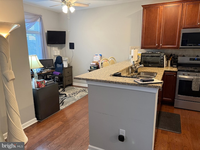 kitchen featuring a toaster, a peninsula, dark wood-style flooring, a sink, and appliances with stainless steel finishes