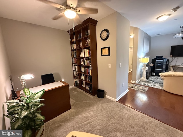 carpeted office space with wood finished floors, a ceiling fan, and baseboards