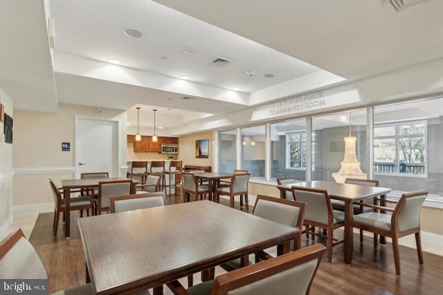 dining area with a tray ceiling, visible vents, baseboards, and wood finished floors