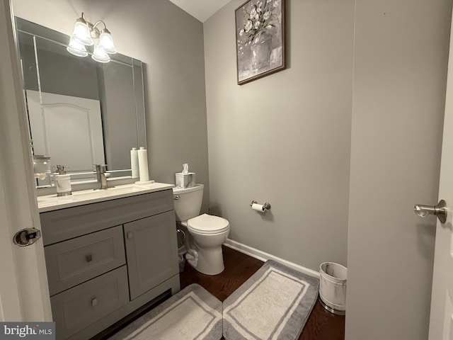 half bathroom featuring baseboards, vanity, toilet, and wood finished floors