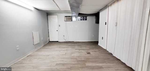 finished basement with an AC wall unit, light wood-type flooring, a paneled ceiling, and baseboards