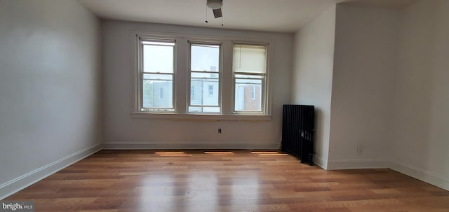 unfurnished room featuring a ceiling fan, radiator, light wood-style flooring, and baseboards