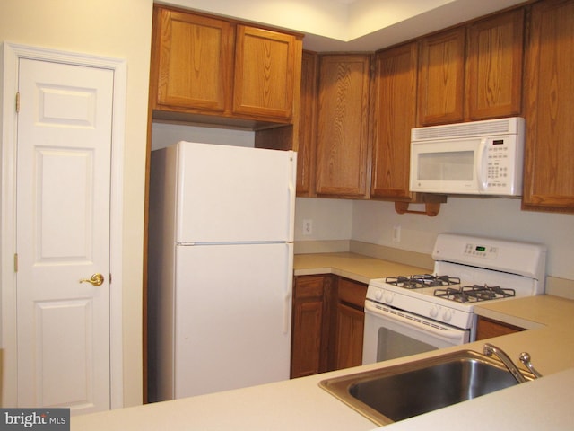 kitchen with brown cabinetry, white appliances, light countertops, and a sink