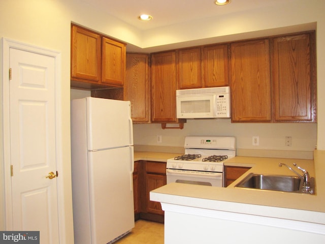 kitchen featuring light countertops, white appliances, brown cabinets, and a sink