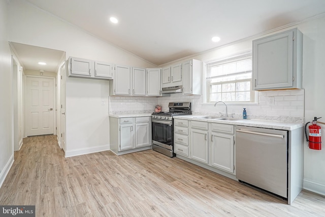 kitchen featuring vaulted ceiling, stainless steel appliances, light countertops, light wood-type flooring, and a sink