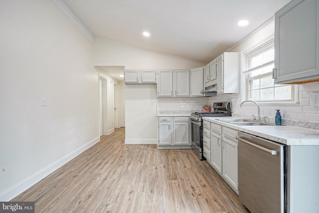 kitchen with lofted ceiling, appliances with stainless steel finishes, a sink, light wood-type flooring, and backsplash