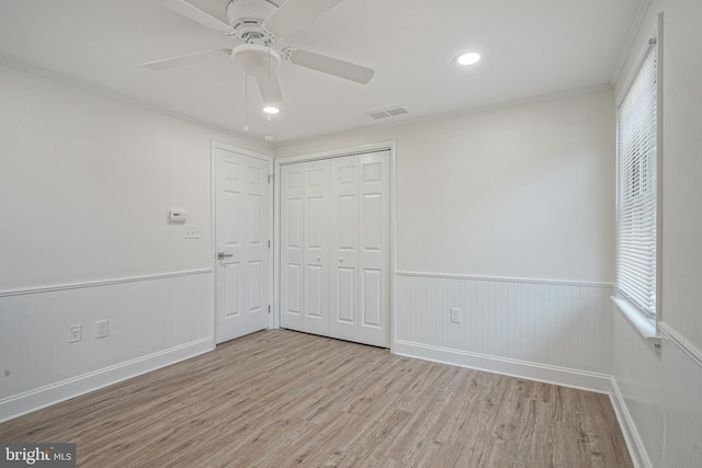 unfurnished bedroom with a wainscoted wall, crown molding, a closet, visible vents, and wood finished floors