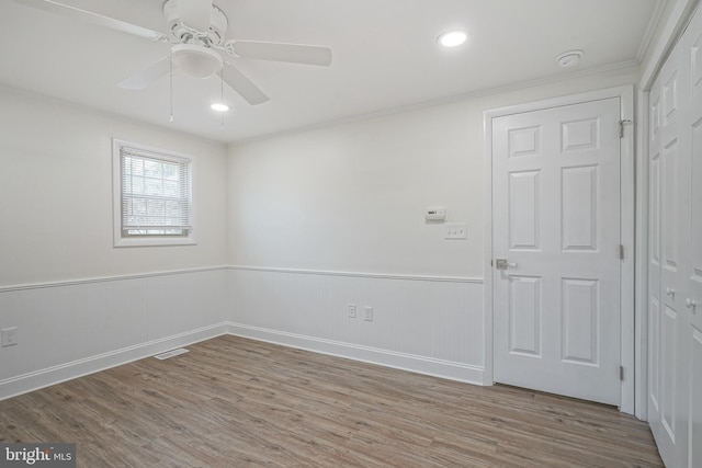 spare room featuring a ceiling fan, a wainscoted wall, visible vents, and wood finished floors