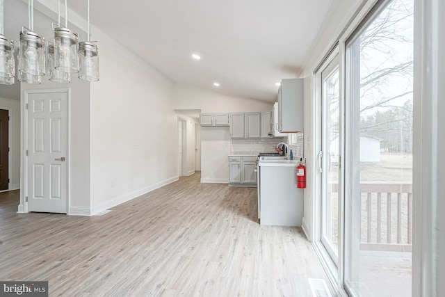 kitchen with light countertops, light wood-style flooring, backsplash, vaulted ceiling, and a sink