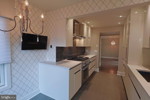 kitchen with stainless steel range, wall chimney range hood, white cabinetry, wallpapered walls, and light countertops