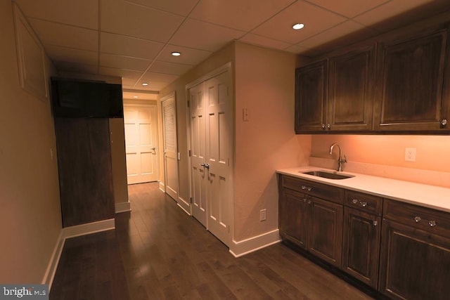 interior space featuring dark wood finished floors, a drop ceiling, baseboards, and a sink