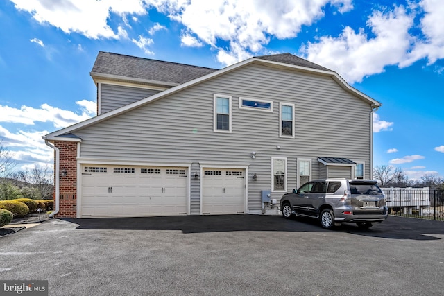 exterior space with aphalt driveway, fence, roof with shingles, an attached garage, and brick siding