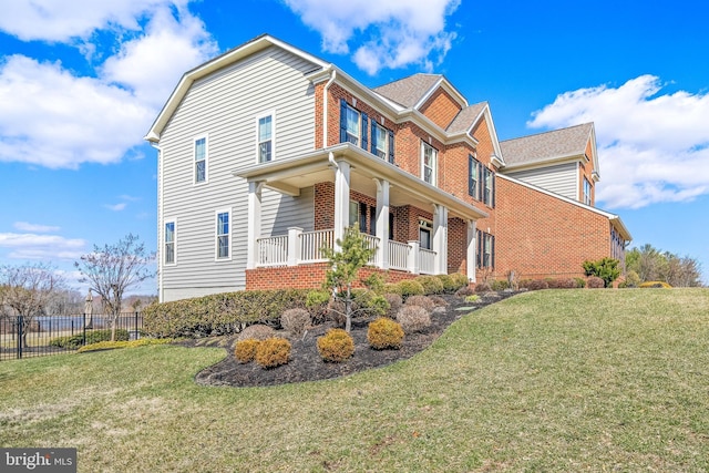 view of side of property featuring brick siding, covered porch, a yard, and fence