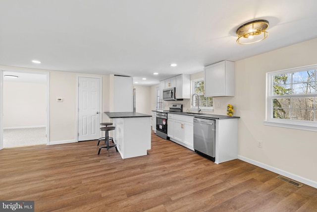 kitchen with visible vents, a sink, a kitchen breakfast bar, dark countertops, and stainless steel appliances