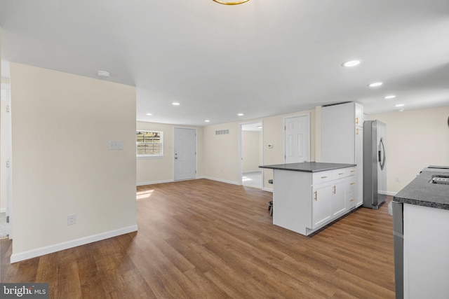 kitchen featuring dark countertops, visible vents, freestanding refrigerator, wood finished floors, and white cabinetry