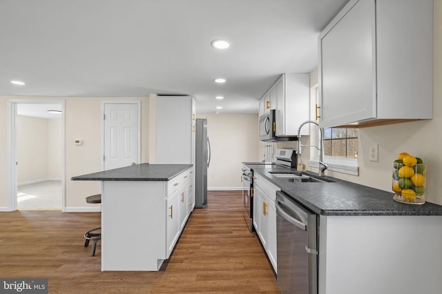 kitchen featuring wood finished floors, a breakfast bar, a sink, appliances with stainless steel finishes, and dark countertops