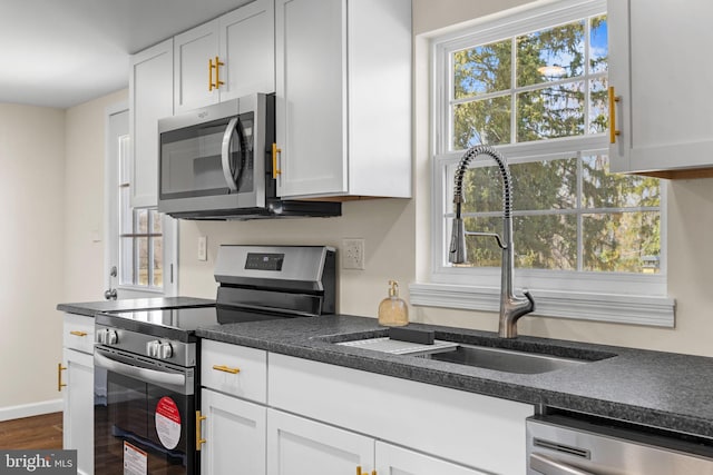 kitchen with dark countertops, white cabinets, appliances with stainless steel finishes, and a sink