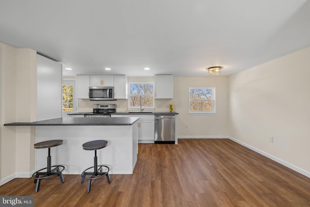 kitchen with dark wood-style flooring, stainless steel appliances, white cabinetry, dark countertops, and a kitchen breakfast bar