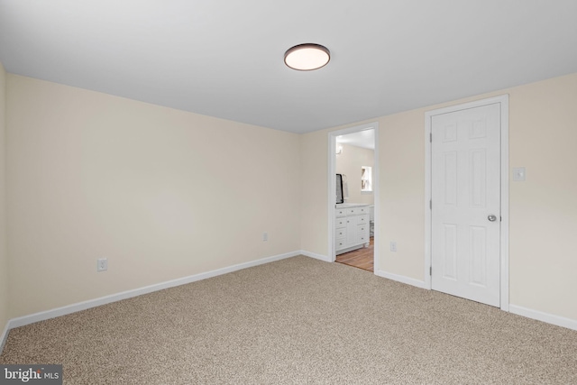 unfurnished bedroom with light colored carpet, ensuite bathroom, and baseboards