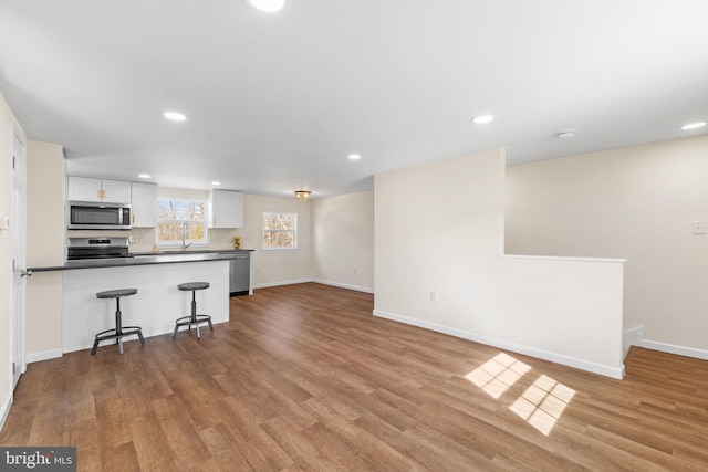 kitchen with a kitchen breakfast bar, dark countertops, wood finished floors, white cabinetry, and stainless steel appliances