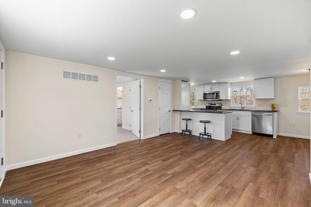 kitchen with dark countertops, visible vents, a breakfast bar, appliances with stainless steel finishes, and wood finished floors