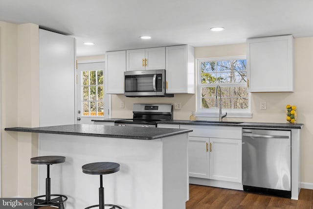 kitchen featuring dark countertops, a kitchen breakfast bar, stainless steel appliances, white cabinetry, and a sink