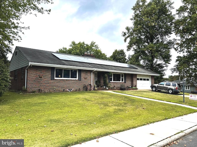 ranch-style house featuring a garage, a front lawn, solar panels, and brick siding