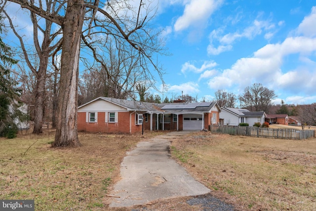 ranch-style house with fence, concrete driveway, a garage, brick siding, and roof mounted solar panels