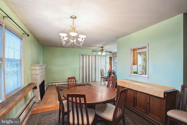 dining room with tile patterned flooring, ceiling fan with notable chandelier, a fireplace, and a baseboard radiator