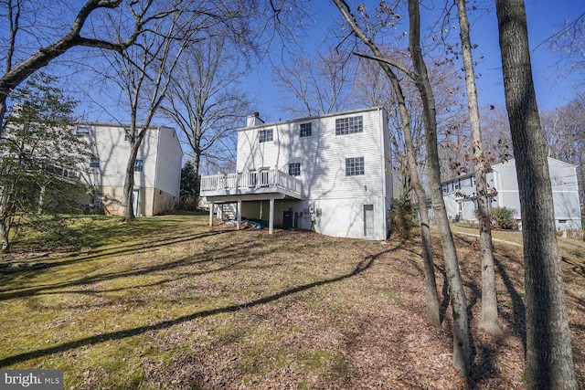 rear view of property with a wooden deck, central AC unit, a lawn, and a chimney