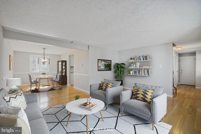 living area with an inviting chandelier, light wood-style floors, baseboards, and a textured ceiling